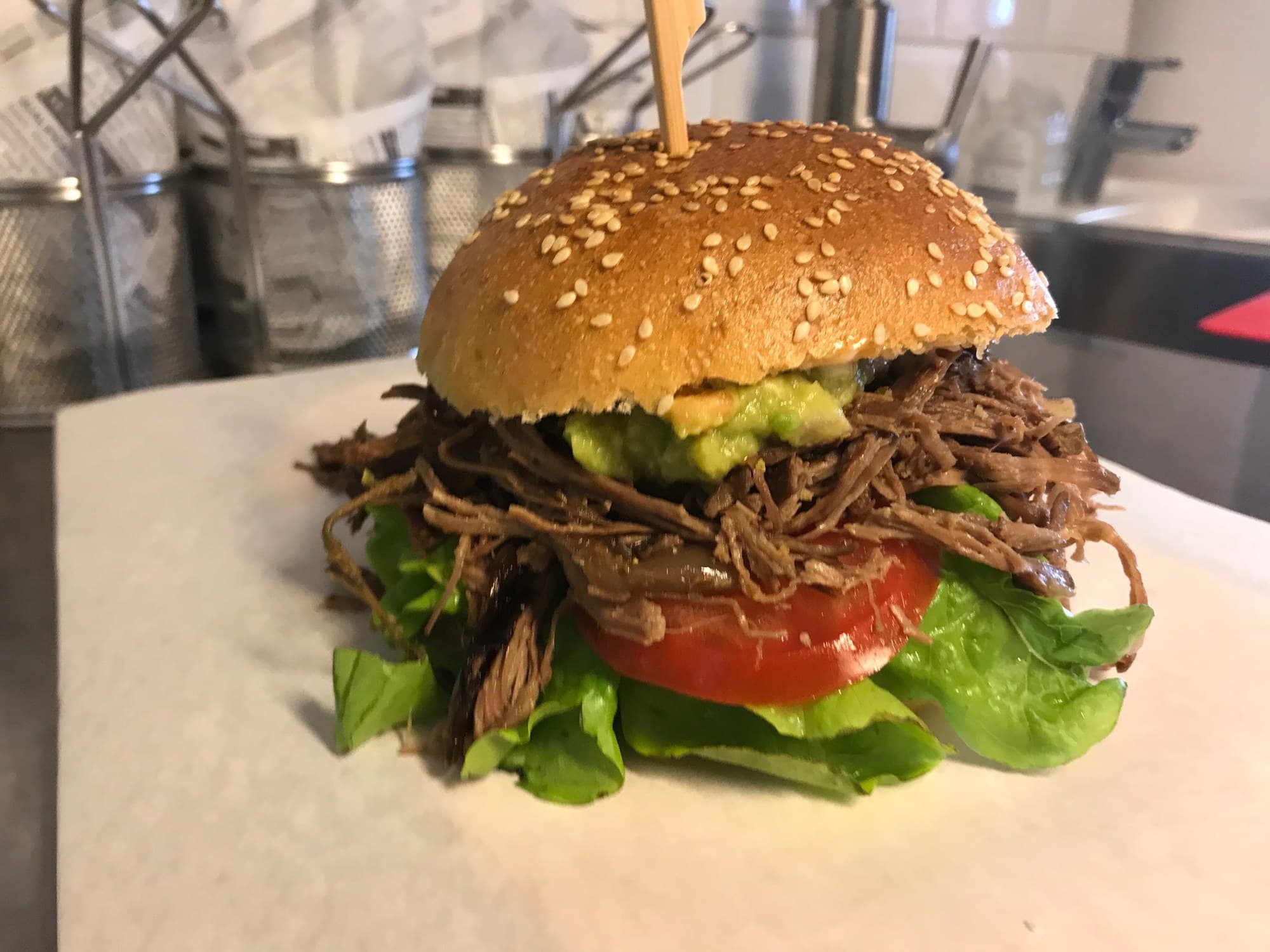 Burger im Sesam-Bun mit gezupftem Fleisch, Guacamole, Tomate und Salat auf hellem Papier