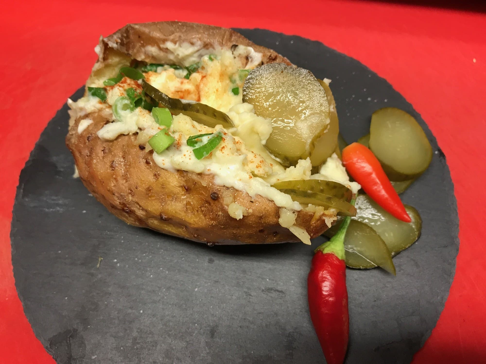 Ofenkartoffel mit heller Füllung, Lauchzwiebeln, Gurkenscheiben und Chilischoten auf einer Schieferplatte